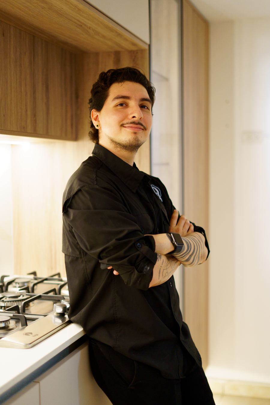 Persona de camisa negra apoyada con los brazos cruzados junto a una cocina a medida con gabinetes de madera